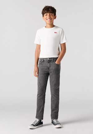 Camiseta de algodón blanca con logo rojo, combinada con jeans de mezclilla grises. Zapatillas altas en blanco y negro. Fondo liso.