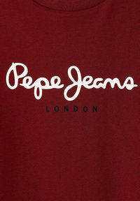Bordová bavlněná trička s velkým bílým kurzívním textem "Pepe Jeans" a menším černým "LONDON" pod ním. Měkká textura. Kulatý výstřih.