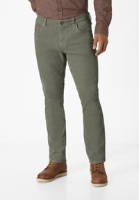 Olive green, slim-fit trousers with a smooth texture, five pockets, and a button closure, paired with brown lace-up boots.