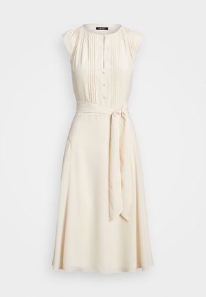 Robe sans manches crème avec boutons sur le devant, détails plissés sur le corsage et ceinture nouée à la taille.