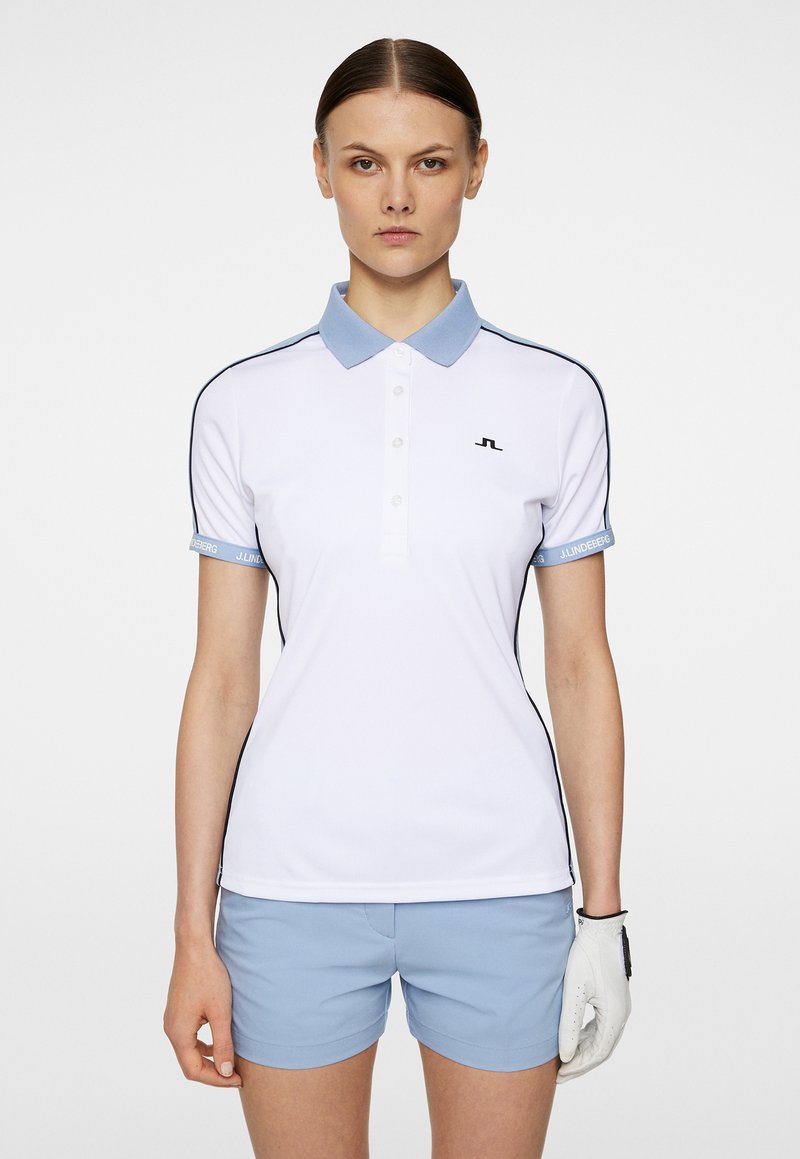 Vit polo skjorta med ljusblå krage och ärmdetaljer, prydd med svarta detaljer och en logotyp på vänster bröst. Kombineras med ljusblå shorts.