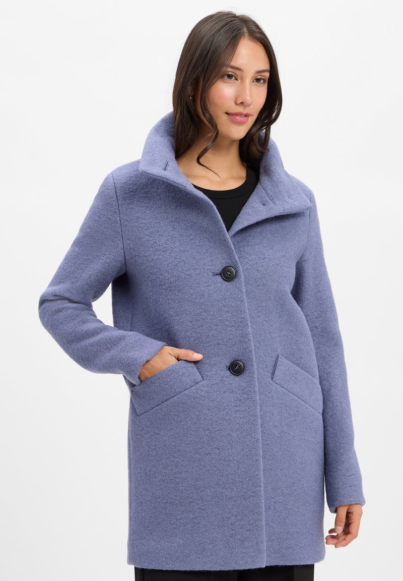 Helle blaue Wolljacke mit hohem Kragen, zwei vorderen Taschen und schwarzen Knöpfen. Der Stoff hat ein weiches, strukturiertes Erscheinungsbild.