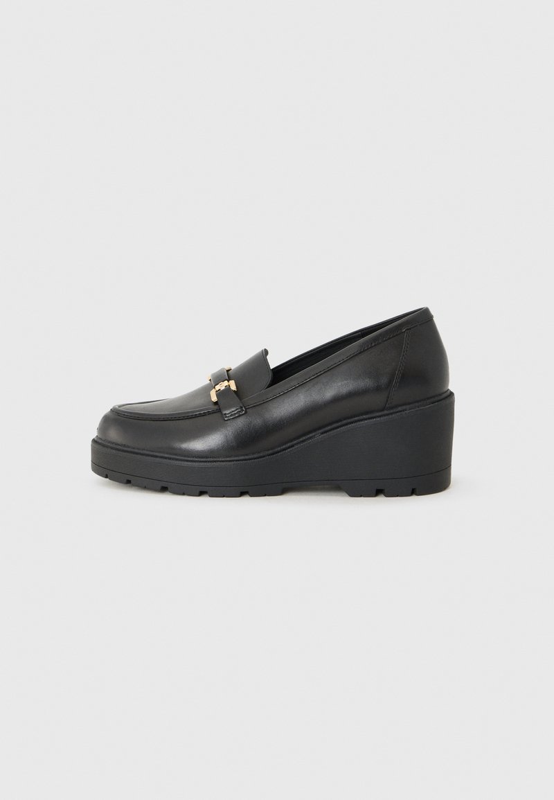 Mocassins noirs à semelle compensée en cuir lisse avec un bout arrondi, comportant un détail décoratif en métal doré à l'avant.