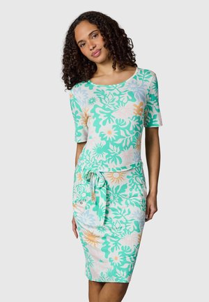 Kobieta nosząca sukienkę do kolan z krótkimi rękawami i kolorowym abstrakcyjnym kwiatowym wzorem w zieleni, niebieskim, brzoskwiniowym i białym, związana w talii.