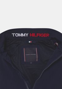 Marinejakke med lynlås foran, mesh-for og broderet "TOMMY HILFIGER" logo i rød og hvid på kraven.