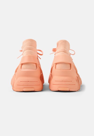 Coral sneakers with a sock-like upper, padded high collar and laces, thick sole with grooves, and textured rear accents.