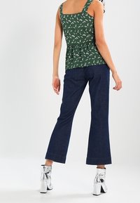 Top verde floral con peplum y escote cuadrado, combinado con pantalones acampanados de mezclilla oscura. Botines plateados brillantes completan el conjunto.