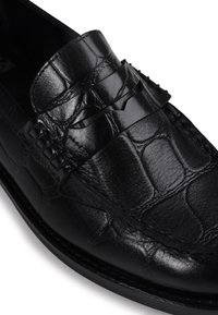 Sapatilha de couro preto com um padrão texturizado de crocodilo, apresentando um design cosido e uma fita decorativa na frente.