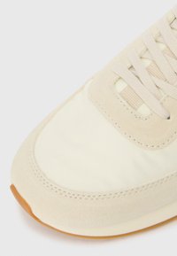 Beżowe sneakersy z połączenia zamszu i gładkiego materiału tekstylnego, okrągłym noskiem oraz gumową podeszwą z jasnobrązowym akcentem.