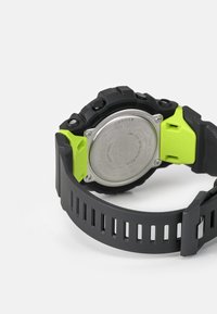 Schwarze Sportuhr mit metallischem Gehäuse, strukturiertem grauen Armband und leuchtend grünen Akzenten. Verfügt über mehrere Tasten für zusätzliche Funktionen.