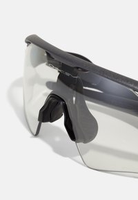 Sonnenbrille mit einem dunklen Rahmen, klaren Gläsern und schwarzen Silikon-Nasenpads. Verfügt über ein elegantes Design und eine schützende Umrandungsform.