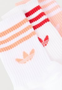 Δύο ζεύγη λευκές ριγωτές κάλτσες με ρίγες στην κορυφή, ένα με ροδακινί ρίγες και λογότυπο, το άλλο με κόκκινες ρίγες και λογότυπο.