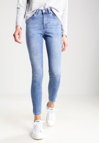 Vaqueros ajustados de color azul claro, hechos de denim, con una cintura alta, bolsillos estándar y un ligero desvanecimiento, combinados con zapatillas blancas.