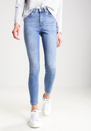 Vaqueros ajustados de color azul claro, hechos de denim, con una cintura alta, bolsillos estándar y un ligero desvanecimiento, combinados con zapatillas blancas.
