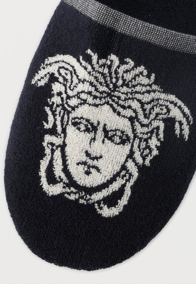 Μαύρο υφασμάτινο με υφή που παρουσιάζει ένα λεπτομερές λευκό μοτίβο κεφαλιού Μέδουσας με μαλλιά σαν φίδια στην περιοχή του δακτύλου ενός παντόφλας.