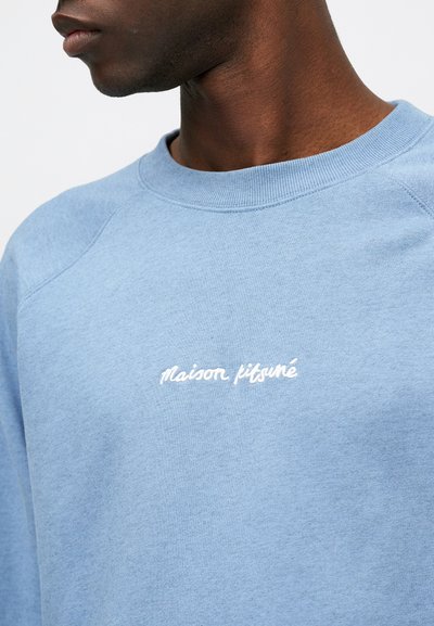 Sudadera azul claro con cuello redondo acanalado, que presenta el texto bordado "maison kitsuné" en blanco en el pecho. Textura suave, diseño casual.