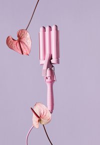 Fer à friser à trois barils avec un corps et une poignée en plastique rose. Il dispose d'une poignée texturée et de boutons. Entouré d'accents floraux roses.
