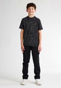 Maglietta nera con grafica a stampa testurizzata, abbinata a pantaloni neri e scarpe da ginnastica bianche. L'outfit presenta una scollatura tonda e maniche corte.