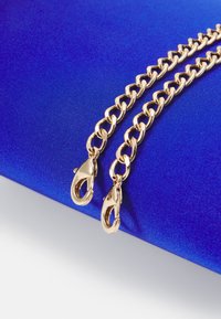 Řetěz s velkými články v zlaté barvě se dvěma karabinkami, ležící na živém modrém saténovém pozadí. Hladký povrch a lesklý povrch.