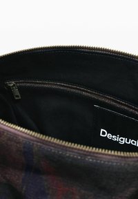 Vista dall'alto dell'interno di una borsa che mostra una tasca con zip e un'etichetta del marchio "Desigual" sulla fodera in tessuto nero.