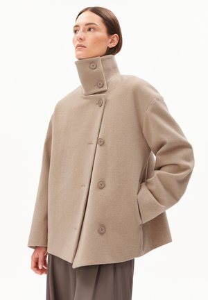 Manteau en laine beige avec un col haut, comportant cinq boutons à l'avant et des manches larges et structurées. Texture lisse et coupe décontractée.