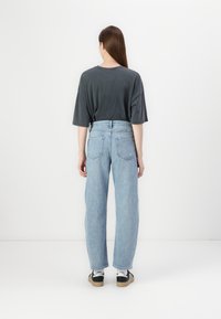 T-shirt gris oversize, jean taille haute bleu clair et baskets noires avec des accents blancs. Fond uni, sans détails supplémentaires.