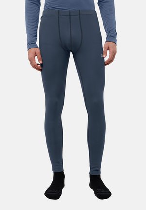 Mann in blauen Thermo-Leggings und Langarmoberteil, der mit entspannt hängenden Händen dasteht, trägt schwarze Socken.