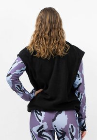 Schwarzes Fleece-Ärmeloberteil, kombiniert mit einem gemusterten lila und blauen Langarmshirt sowie Leggings, die kühne abstrakte Designs zeigen.