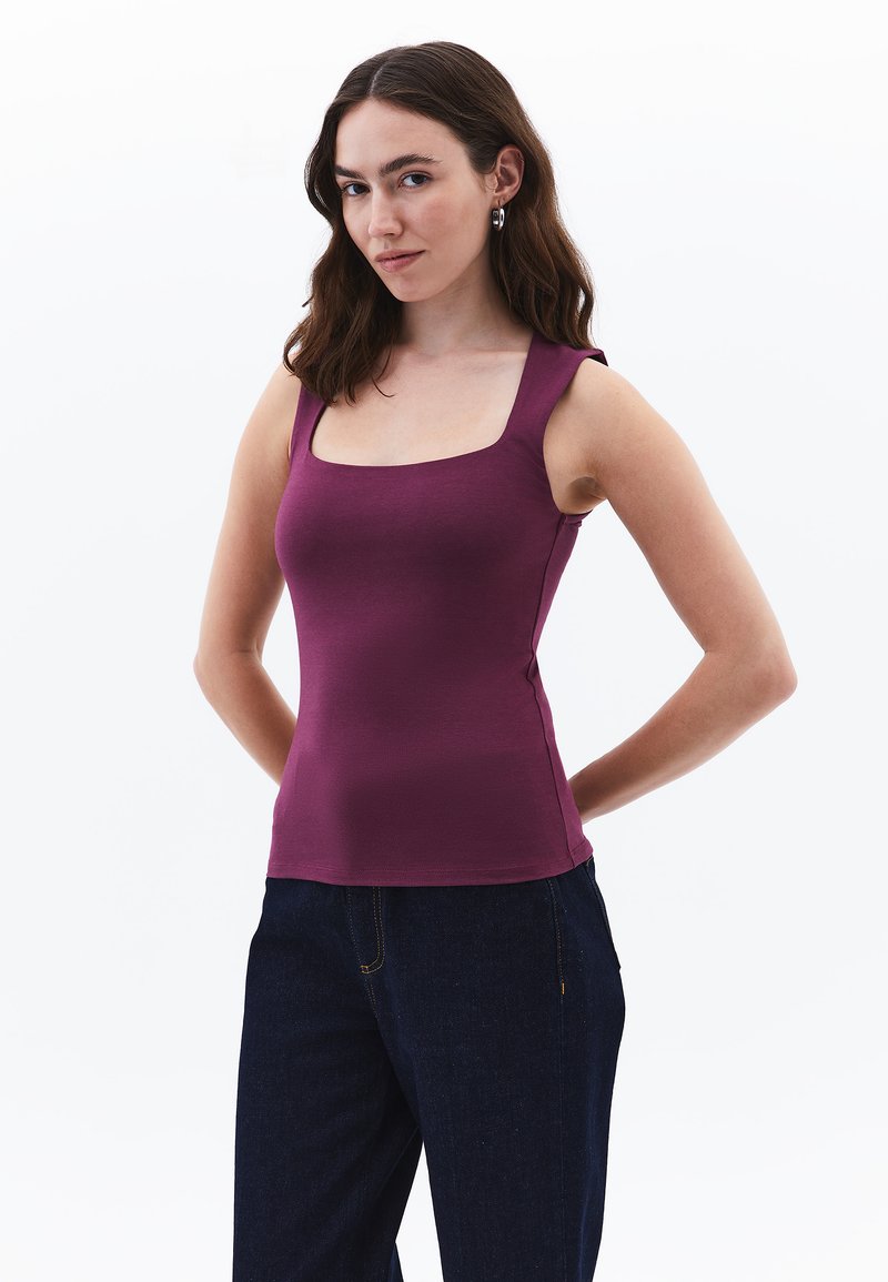 Top de tirantes ajustado color burdeos con escote cuadrado y tirantes gruesos, fabricado en una tela suave. Combinado con jeans azul oscuro con bolsillos laterales.