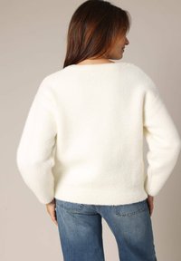 Witte, donzige wollen trui met een ronde hals en verlaagde schouders, gecombineerd met blauwe denim jeans. Getextureerd oppervlak, losse pasvorm.