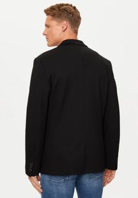 Blazer nero con un design su misura e una texture liscia. Presenta un colletto a rever, maniche lunghe e dettagli a bottone sui polsini.