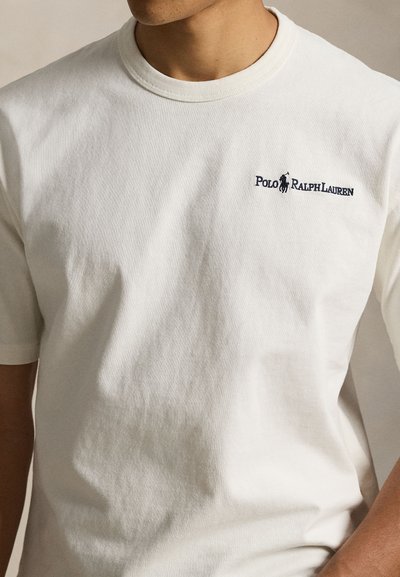 Μπεζ βαμβακερή μπλούζα με στρογγυλή λαιμόκοψη και κοντά μανίκια. Διαθέτει κεντητό σκούρο μπλε λογότυπο "Polo Ralph Lauren" στο στήθος.