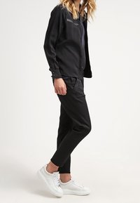 Czarna koszula z długimi rękawami i kieszenią z przodu, w połączeniu z czarnymi zwężanymi spodniami i białymi trampkami. Gładki, lekki materiał.