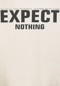 White T-shirt with bold black text reading "EXPECT NOTHING." Additional smaller black text above the main phrase. Fabric appears soft.