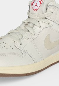 Λευκό δερμάτινο αθλητικό παπούτσι Air Jordan με μπεζ σόλα, καφέ εξωτερική σόλα και κόκκινο λογότυπο Jumpman στη γλώσσα.