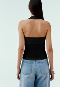 Černý top s halter krkem a úzkým střihem, doplněný světle modrými džíny s vysokým pasem v klasickém pětikapsovém stylu.