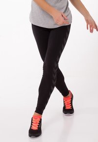 Czarne legginsy o gładkiej strukturze, z delikatnym wzorem w zygzak po bokach. W zestawie z czarnymi sneakersami i jaskraworóżowymi sznurowadłami.