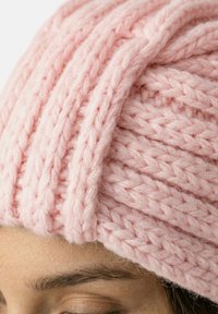 Pink strikket hue med et tekstureret, ribbet mønster, lavet af tykt garn. Fokus på blødt, chunky stof og synlige sy-detaljer.