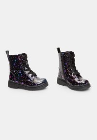 Botas de tobillo de charol negro con un patrón de estrellas en púrpura y azul, diseño con cordones y un cierre lateral para facilitar el uso.