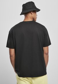 Sort bomulds T-shirt med en afslappet pasform, rund hals og korte ærmer. Sammen med en sort bucket hat. Bagfra ses en subtil stoftekstur.