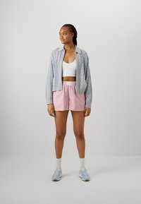 Cardigan de punto con cremallera en azul claro sobre una blusa corta blanca, combinado con pantalones cortos a rayas rosas y zapatillas azul claro. Un conjunto simple y casual.