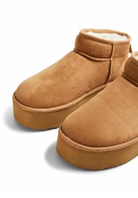 Botines de ante marrón con forro suave, punta redonda y suela de goma gruesa. Presenta detalles de costura y una tira en la parte posterior para facilitar su colocación.