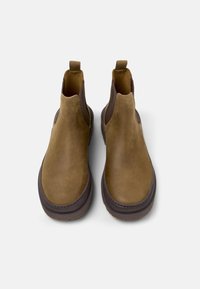 Stivaletti alla caviglia in suede marrone con pannelli elastici laterali, punta arrotondata e suola in gomma spessa. Comprendono linguette per facilitare l'indossamento.