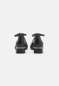Chaussures en cuir noir avec un bout arrondi, une sangle à la cheville, des accents cloutés et un talon bloc avec une bordure dorée.