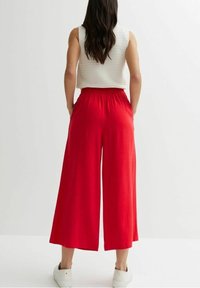 Red wide-leg trousers with a relaxed fit, made from light fabric, featuring a drawstring waist and pockets, paired with a white sleeveless top.