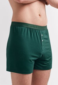 Grüne Baumwollboxershorts mit einem weichen Bund und geprägt Text, zwei Knöpfen an der Vorderseite und einem glatten, anliegenden Design.