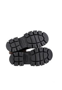 Black rubber boot soles with deep treads, featuring a textured surface and alternating rectangular and round patterns for traction.