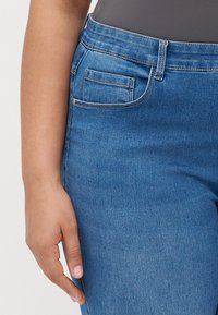 Vidutinio mėlynumo džinsai, su liesu kirpimu, klasikinio penkių kišenių dizaino ir subtilių siuvimo detalių.