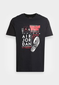 Camiseta de algodón negra con un diseño gráfico que incluye el texto "AIR JORDAN", acentos rojos y una impresión de suela de zapato. Mangas cortas, cuello redondo.