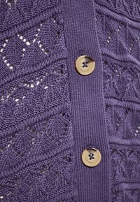 Cardigan tricotat de culoare mov, cu un design texturat și modele în formă de diamant, evidențiat de nasturi mari de culoare crem pe față.